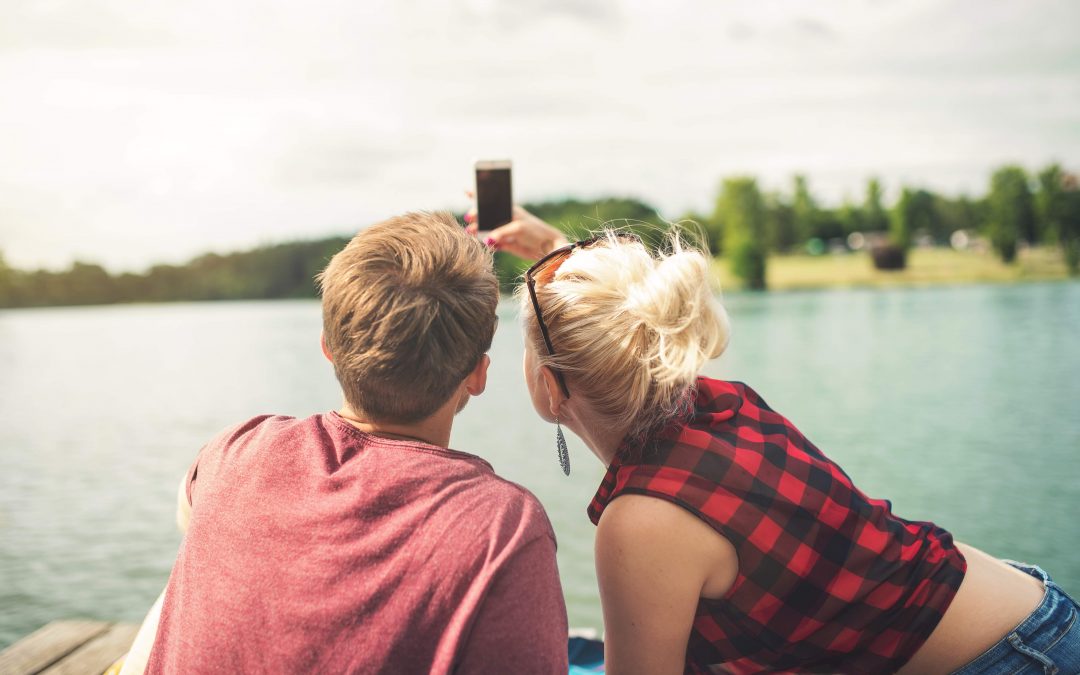 Two young adults taking a picture of the lake from on a dock.