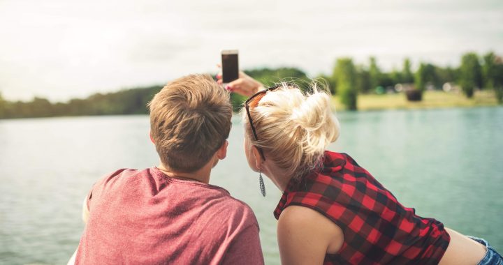 Two young adults taking a picture of the lake from on a dock.